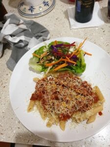white plate with penne bolognese with cheese on top, with a side salad